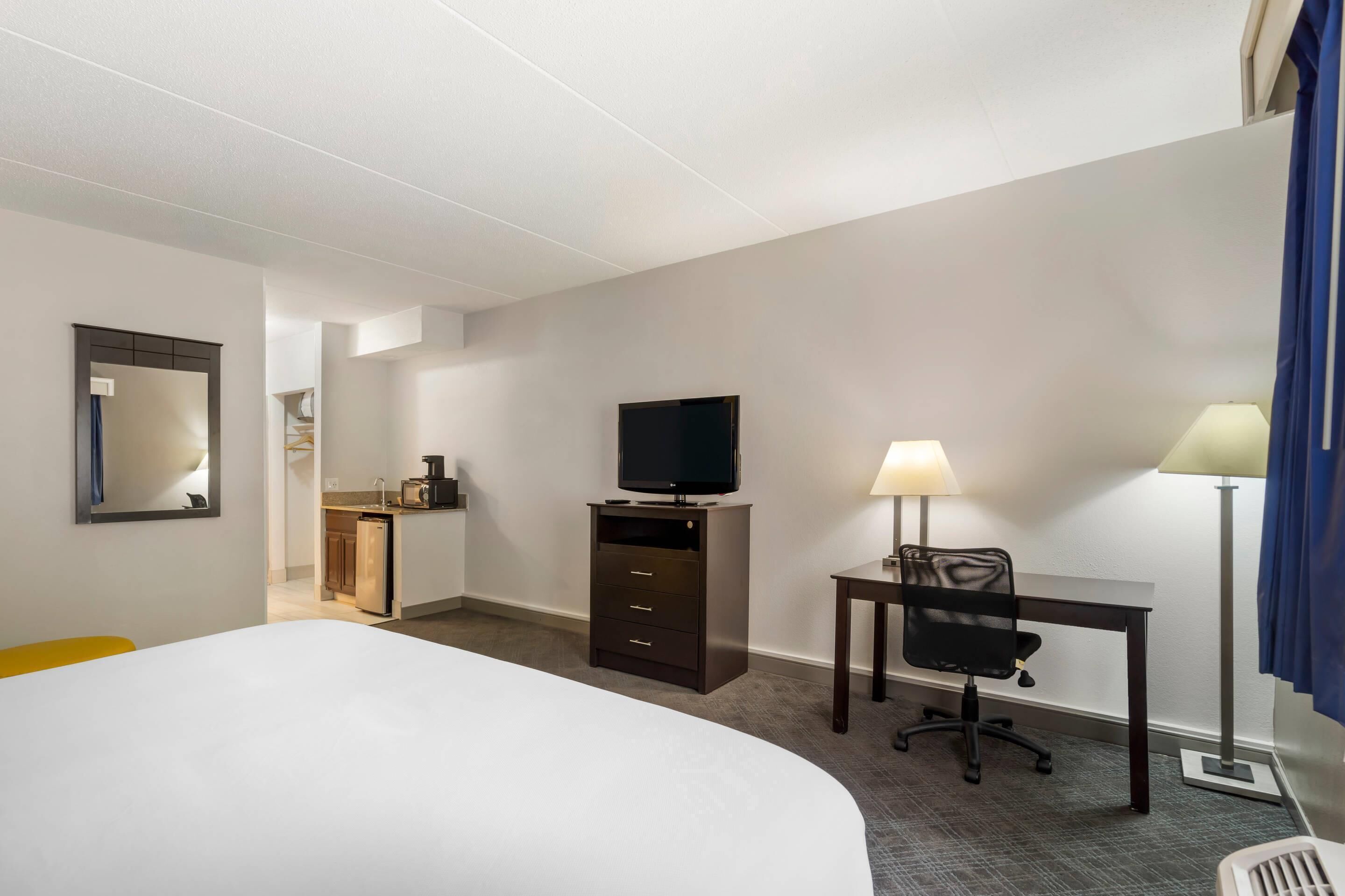 Ett hotellrum med en säng, ett skrivbord med en stol, en tv och en lampa.