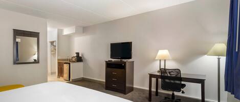 A hotel room with a bed, a desk with a chair, a television, and a lamp.