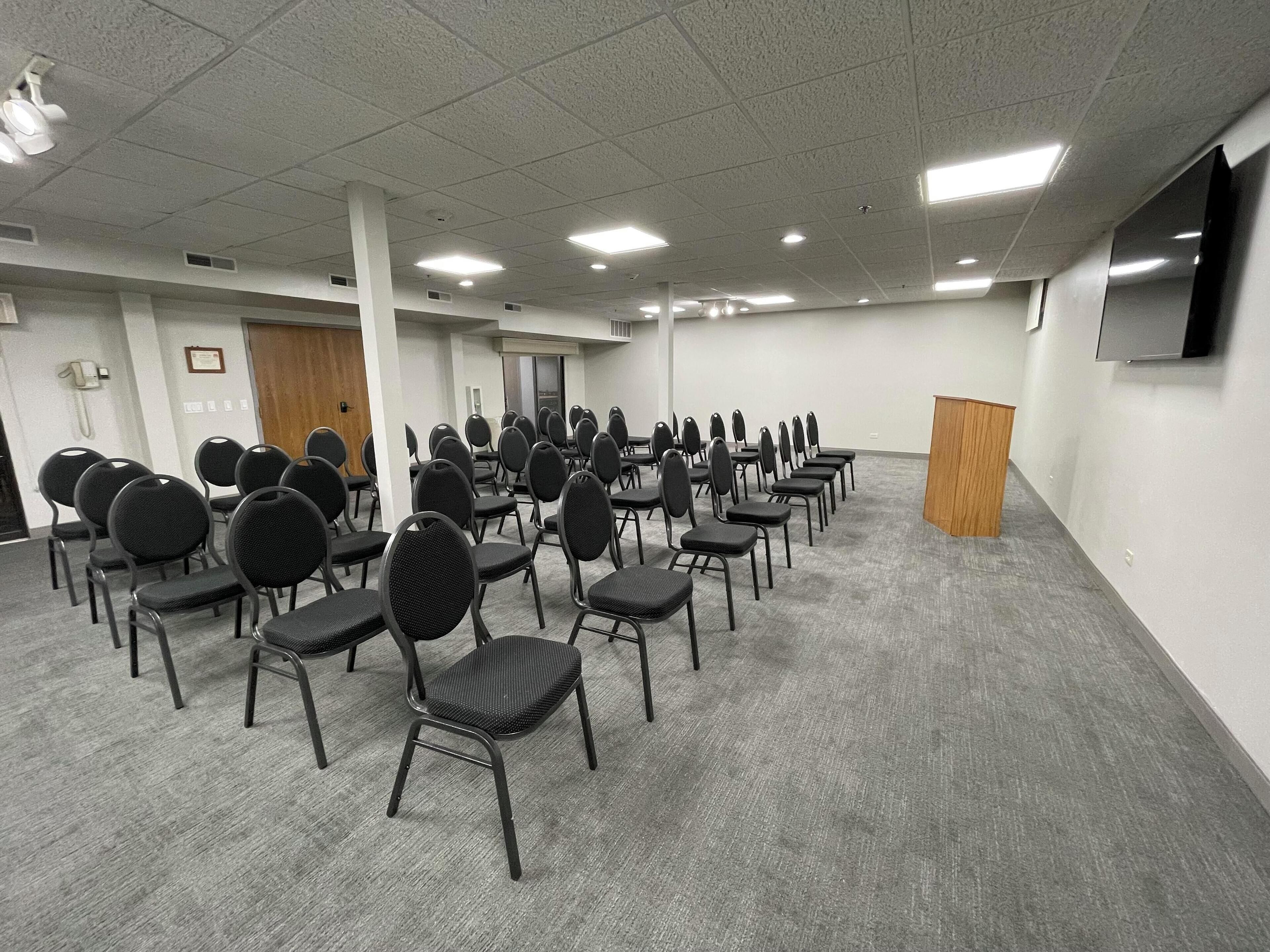 A conference room with rows of chairs, a podium, and a phone on the wall.