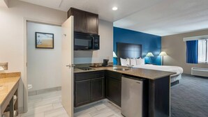 Habitación de hotel pequeña con kitchenette, cama, escritorio y baño.