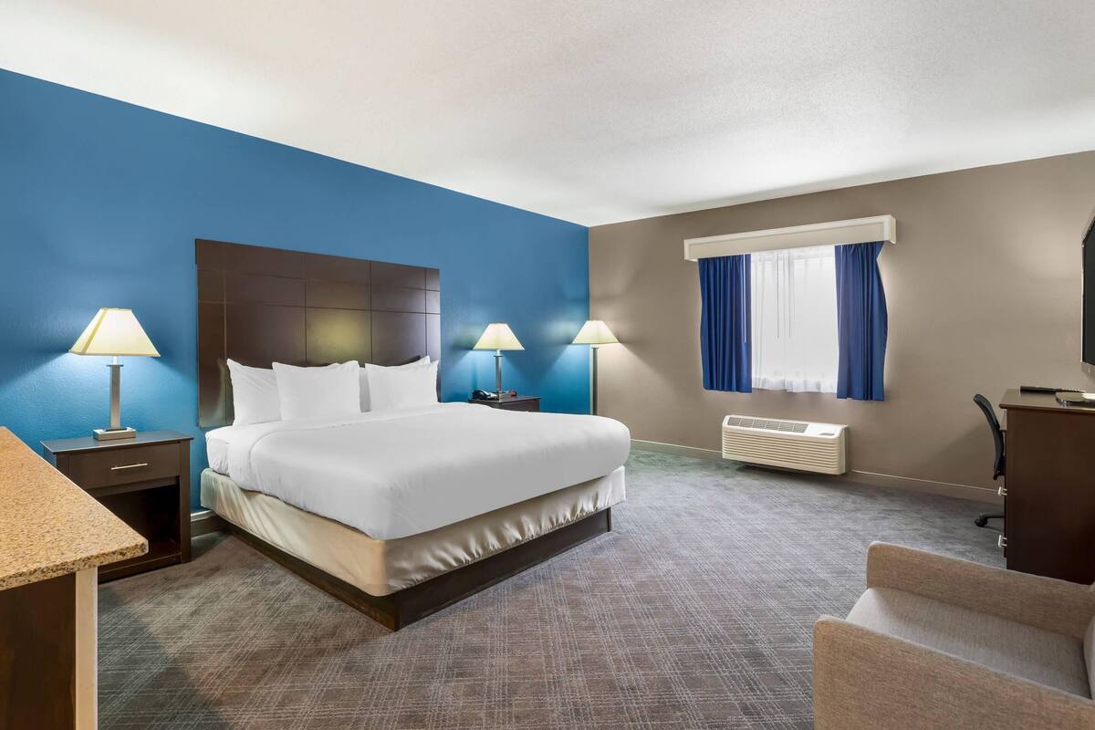 A hotel room with a large bed, two bedside lamps, a desk, a chair, a TV, and a window with curtains.