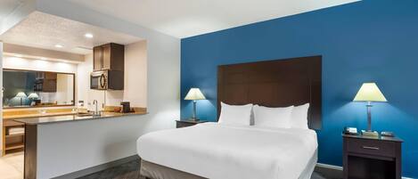 A hotel room with a large bed, a bathroom with a mirror, and a kitchenette.