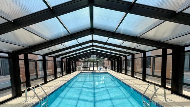 Una piscina techada con paredes de vidrio, barandales de metal y piso de baldosas.