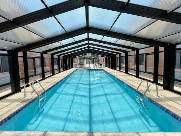 A covered swimming pool with glass walls, metal railings, and a tiled floor.