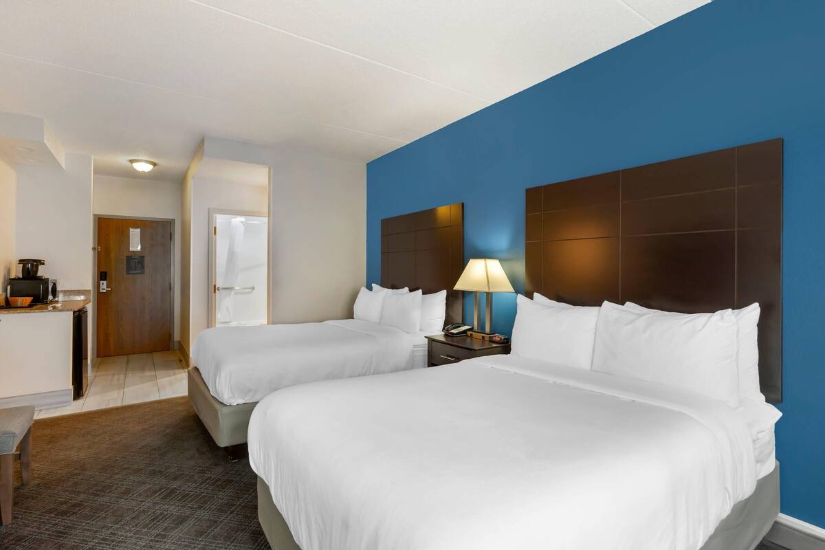 A hotel room with two beds, a desk, a lamp, and a blue accent wall.