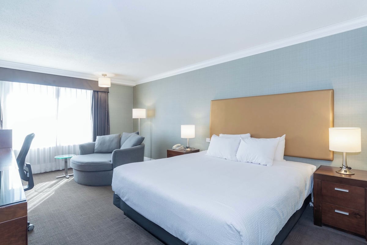 A hotel room with a large bed, a desk, a chair, and a nightstand with a lamp.