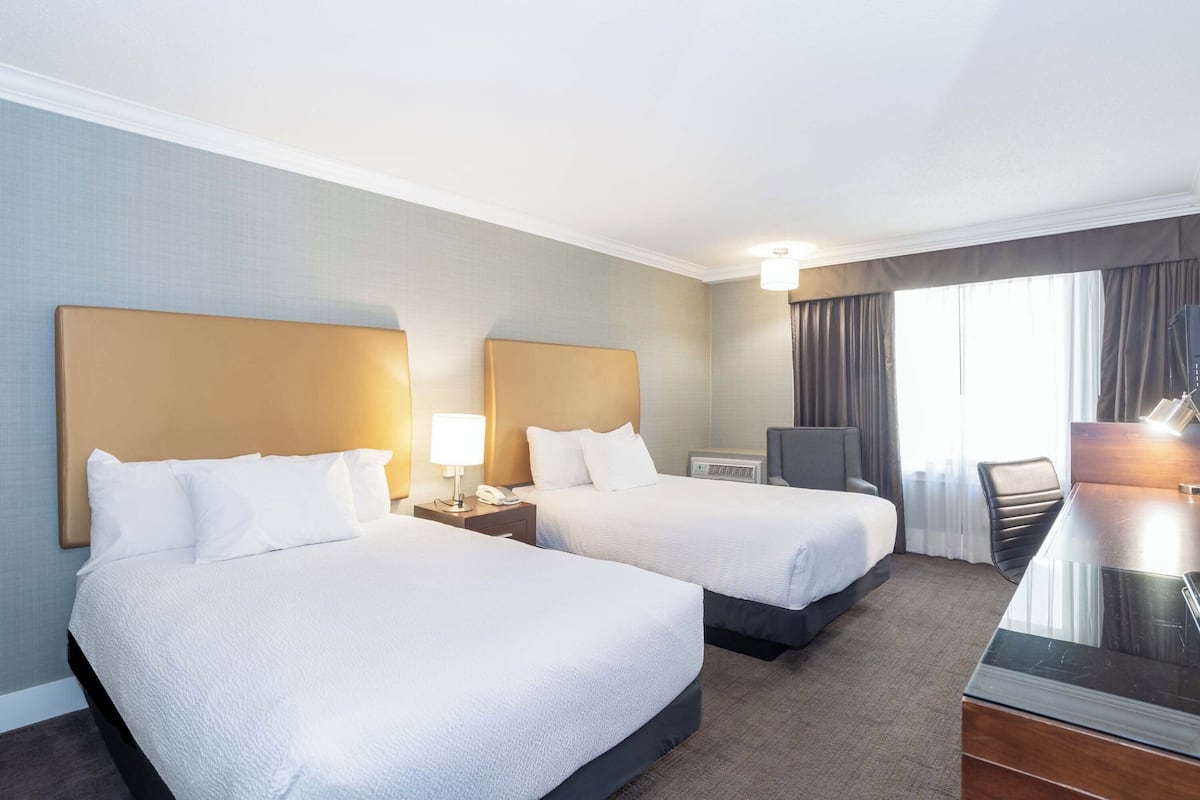 A hotel room with two beds, a desk, a chair, and a window with curtains.