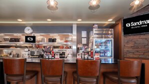 Una zona de bar con cuatro taburetes, un reloj, un refrigerador lleno de bebidas y un letrero de Sandman Inn & Suites.
