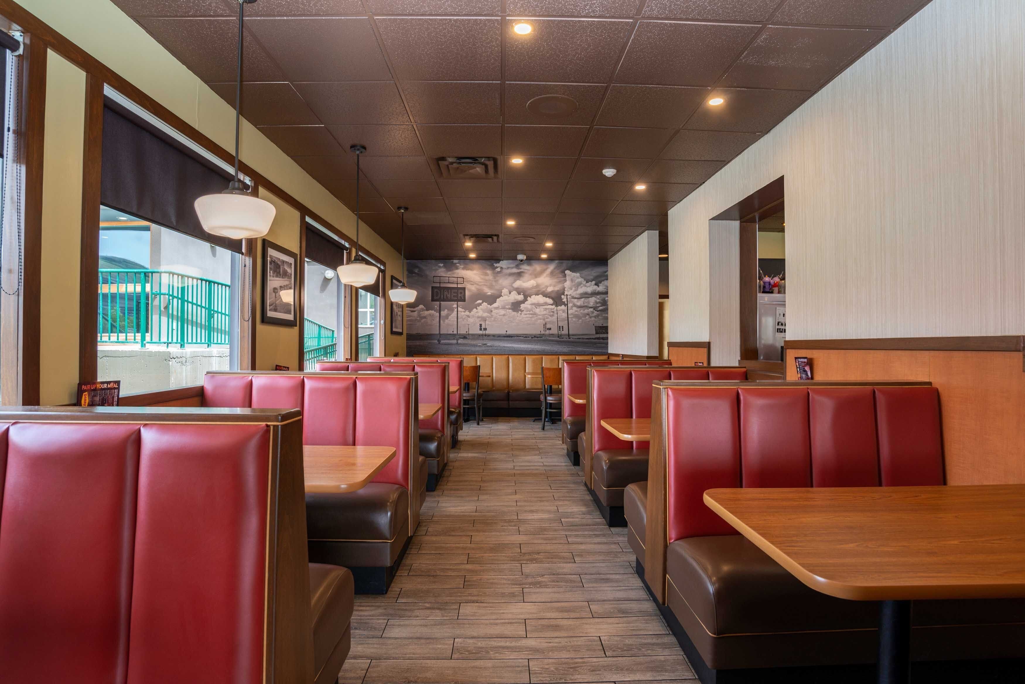 A restaurant interior with booths and tables, a mural on the wall, and a view of the outside.