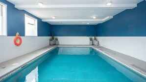 Una piscina con agua azul cristalina, rodeada de paredes de azulejos blancos y detalles azules.