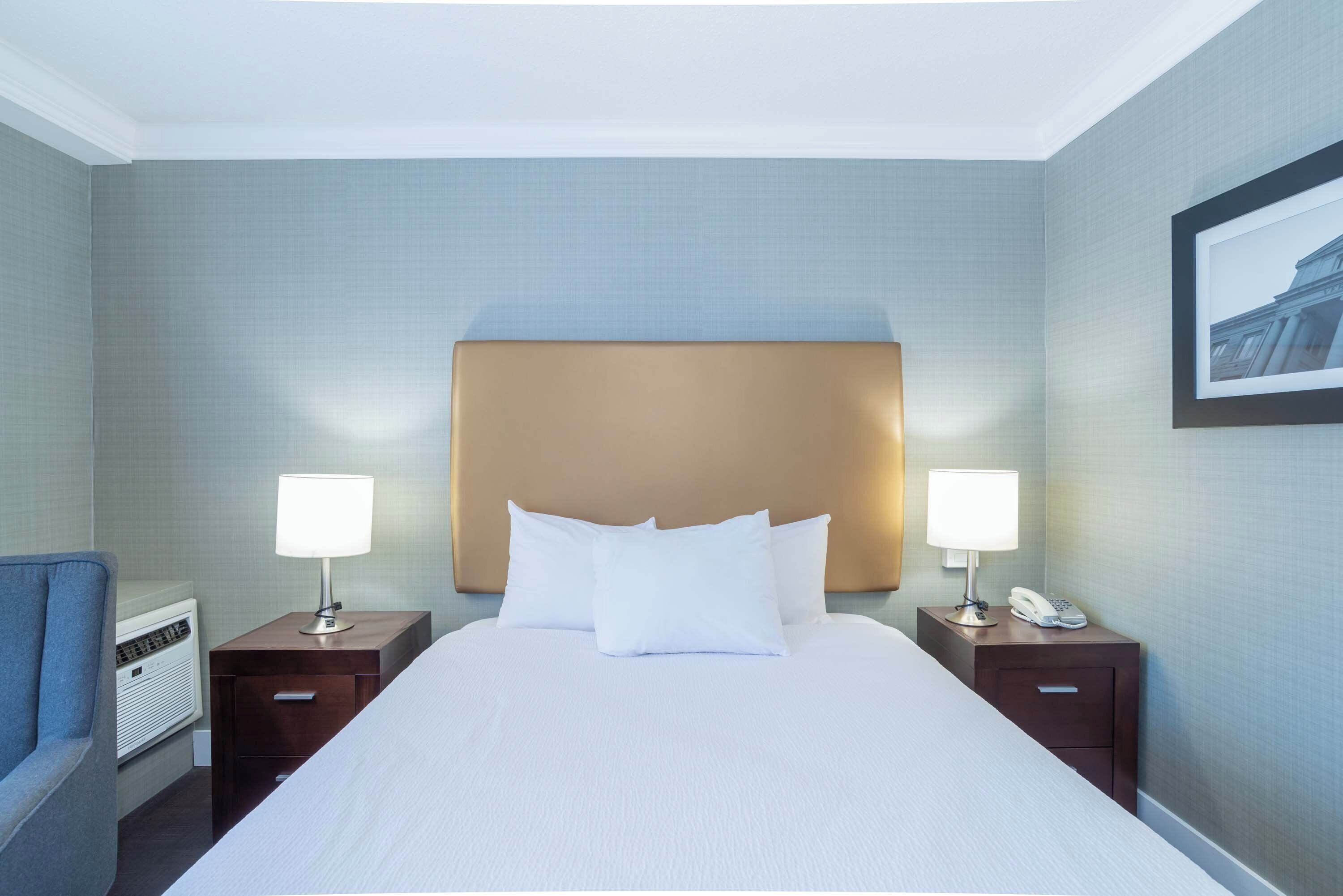 A hotel room with a large bed, two bedside tables with lamps, a chair, and a framed picture on the wall.