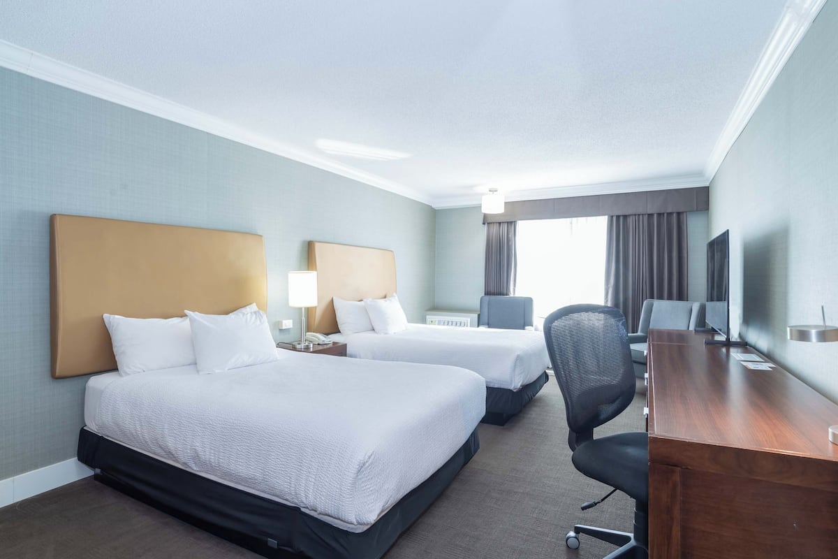 A hotel room with two beds, a desk, a chair, a TV, and a window with curtains.
