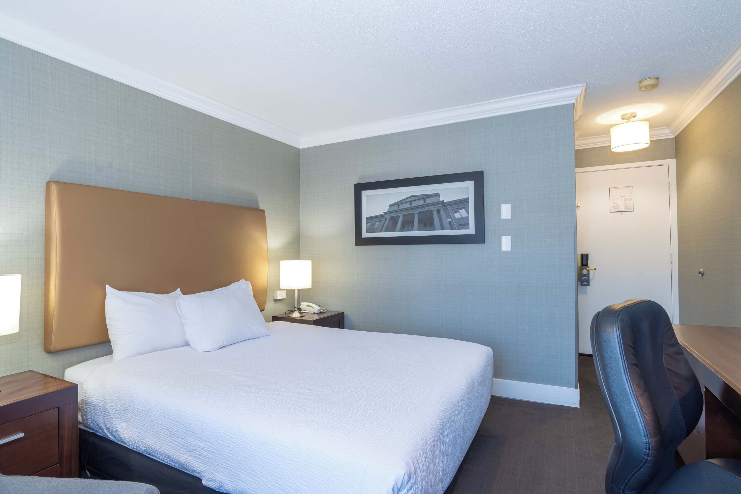 A hotel room with a large bed, bedside lamps, a framed picture on the wall, and a desk with a chair.
