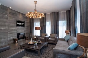A modern living room with a flat-screen TV, a chandelier, and a sofa with cushions. - Sandman Hotel Vernon (Vernon)