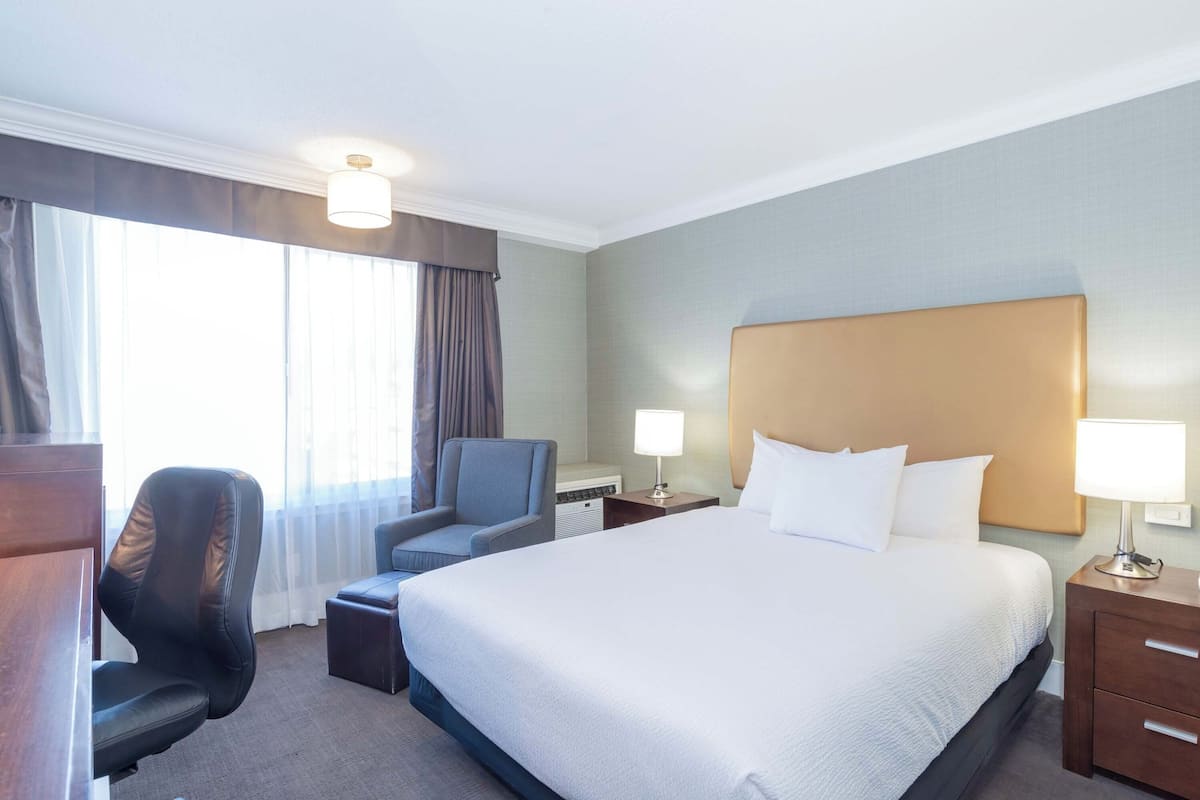 A hotel room with a large bed, a desk, a chair, and a nightstand with lamps.