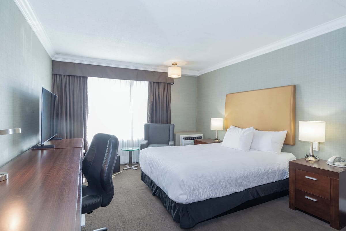A hotel room with a large bed, a desk, a chair, a TV, a lamp, and a bedside table.