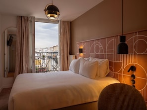 A hotel room with a large bed, a view of the cityscape through the window, and a modern headboard with wall-mounted lights. - Mercure Paris Opéra Faubourg Montmartre (Paris)