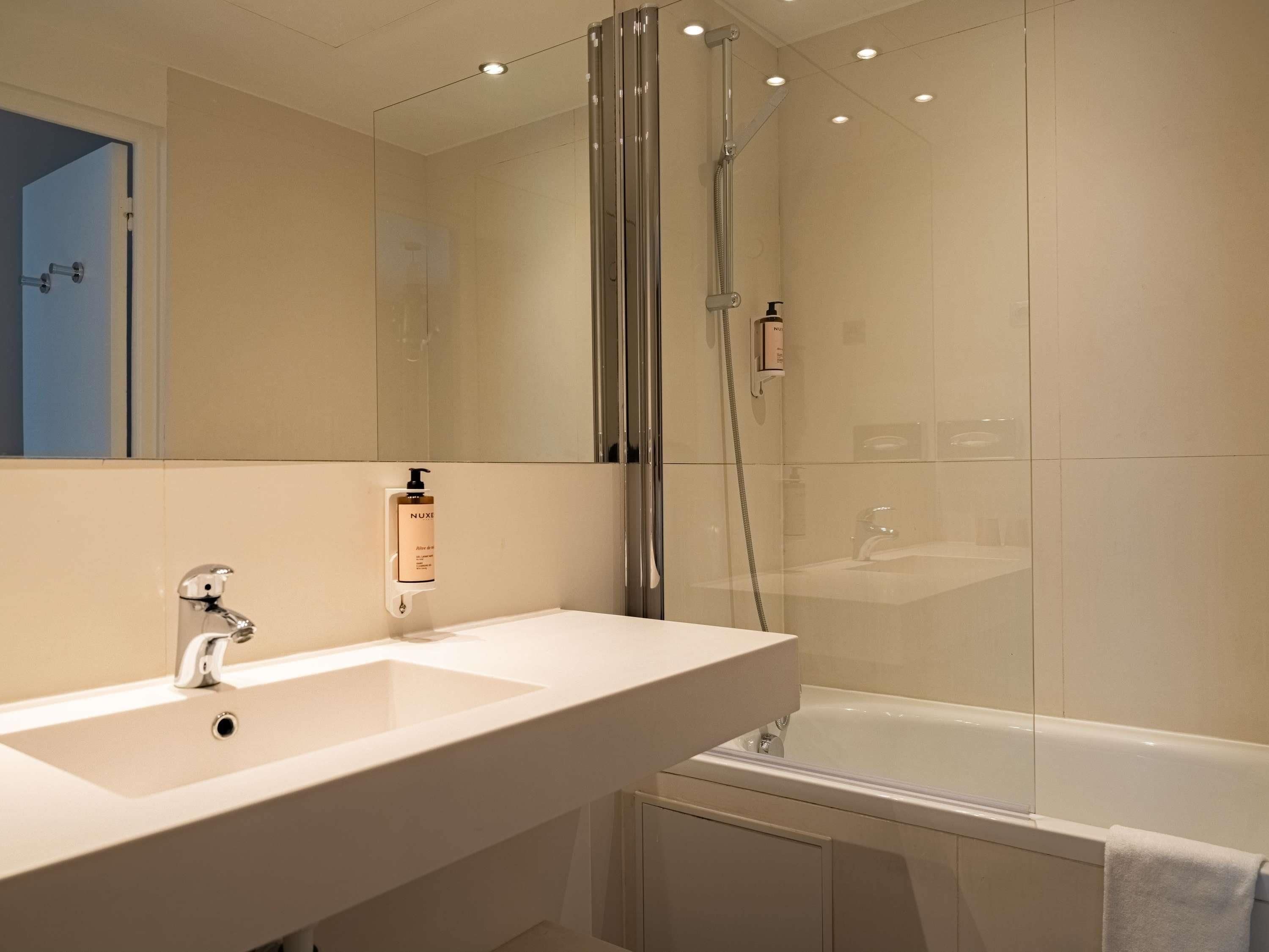 A modern bathroom with a large mirror, a sink, a shower enclosure, and a bathtub.