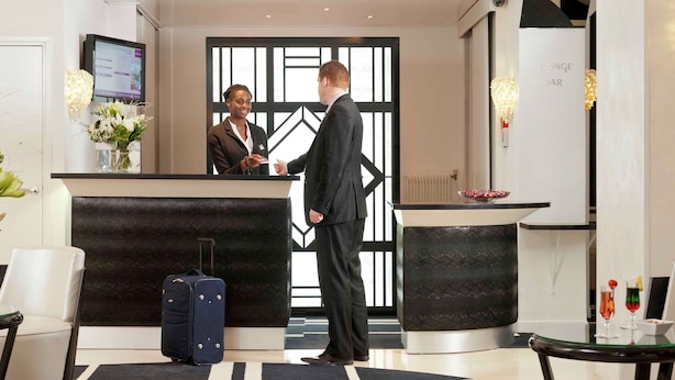 A hotel reception area with a reception desk, a blue suitcase, and a lounge bar. - Mercure Paris Opéra Faubourg Montmartre (Paris)