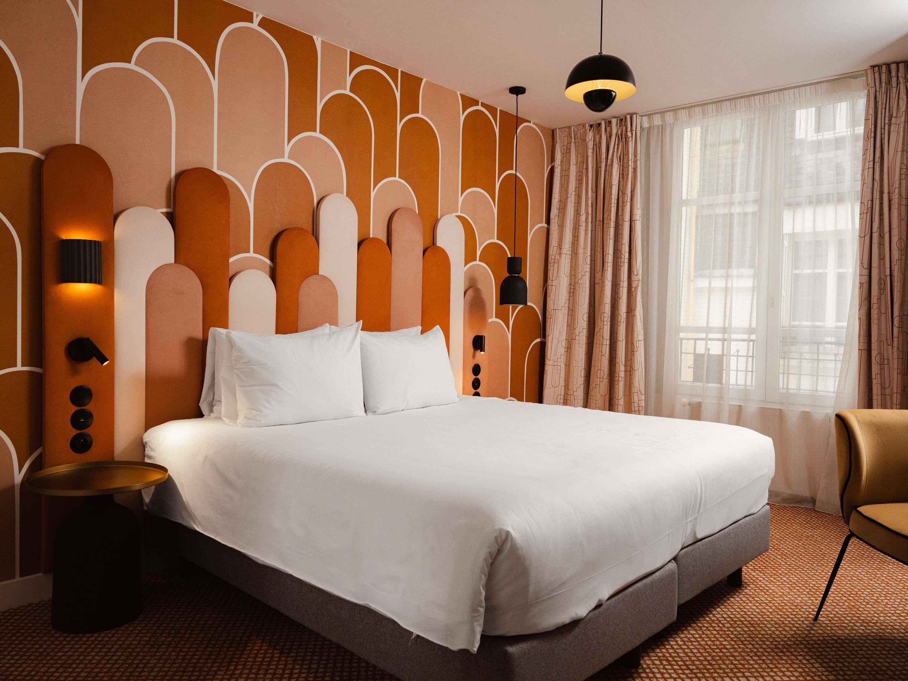 Habitación de hotel con una cama grande, una mesita de noche, una silla y una ventana con cortinas.