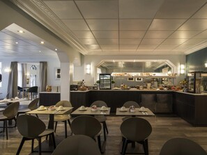A modern dining area with tables, chairs, a kitchen counter, and a view of the dining area. - Mercure Paris Opéra Faubourg Montmartre (Paris)
