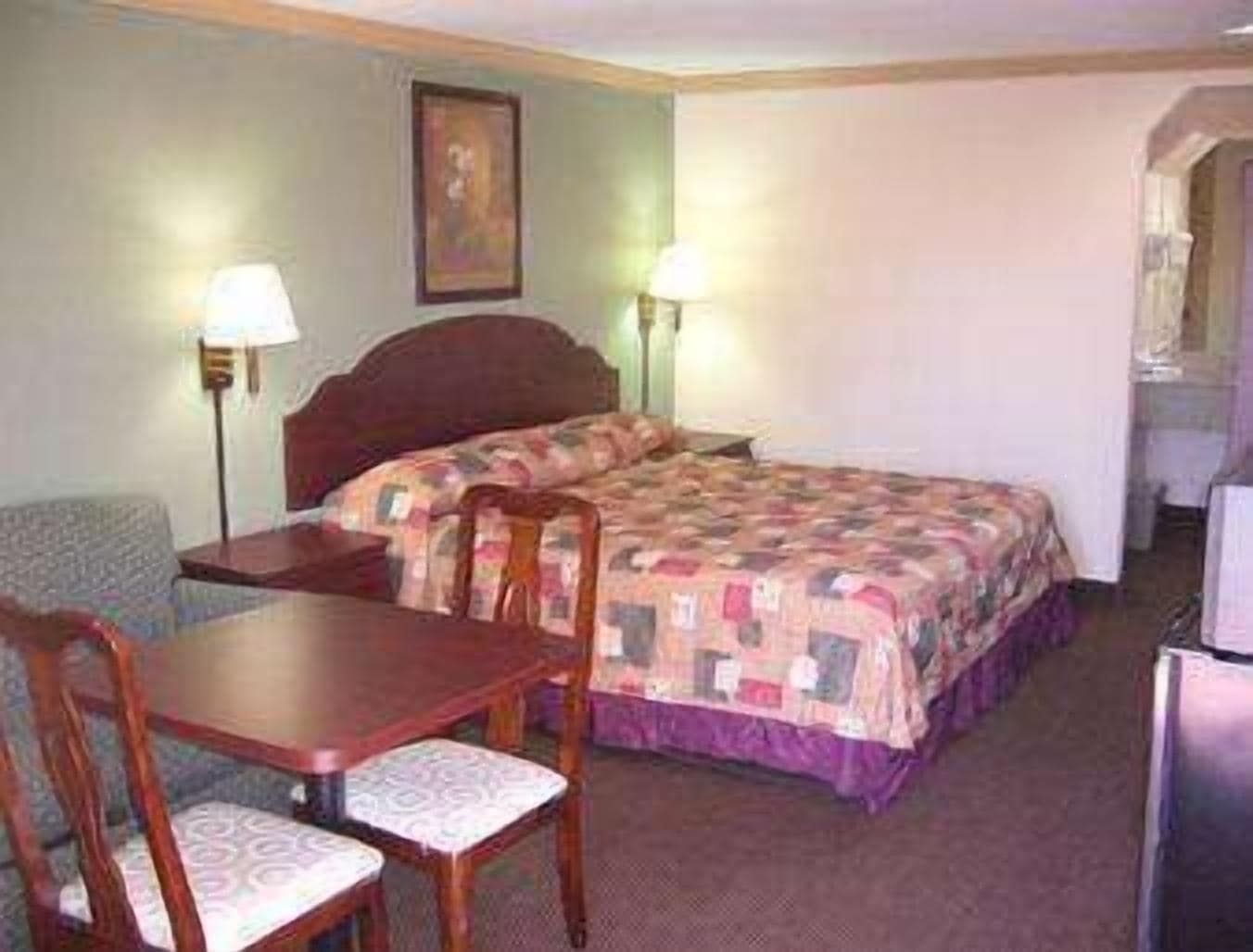 A hotel room with a bed, a desk, a chair, and a lamp.