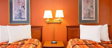 A hotel room with two beds, a nightstand, a lamp, and two framed pictures on the wall.
