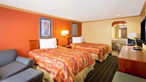 Habitación de hotel con dos camas, un escritorio, una silla, un televisor y un baño visible a través de un arco.