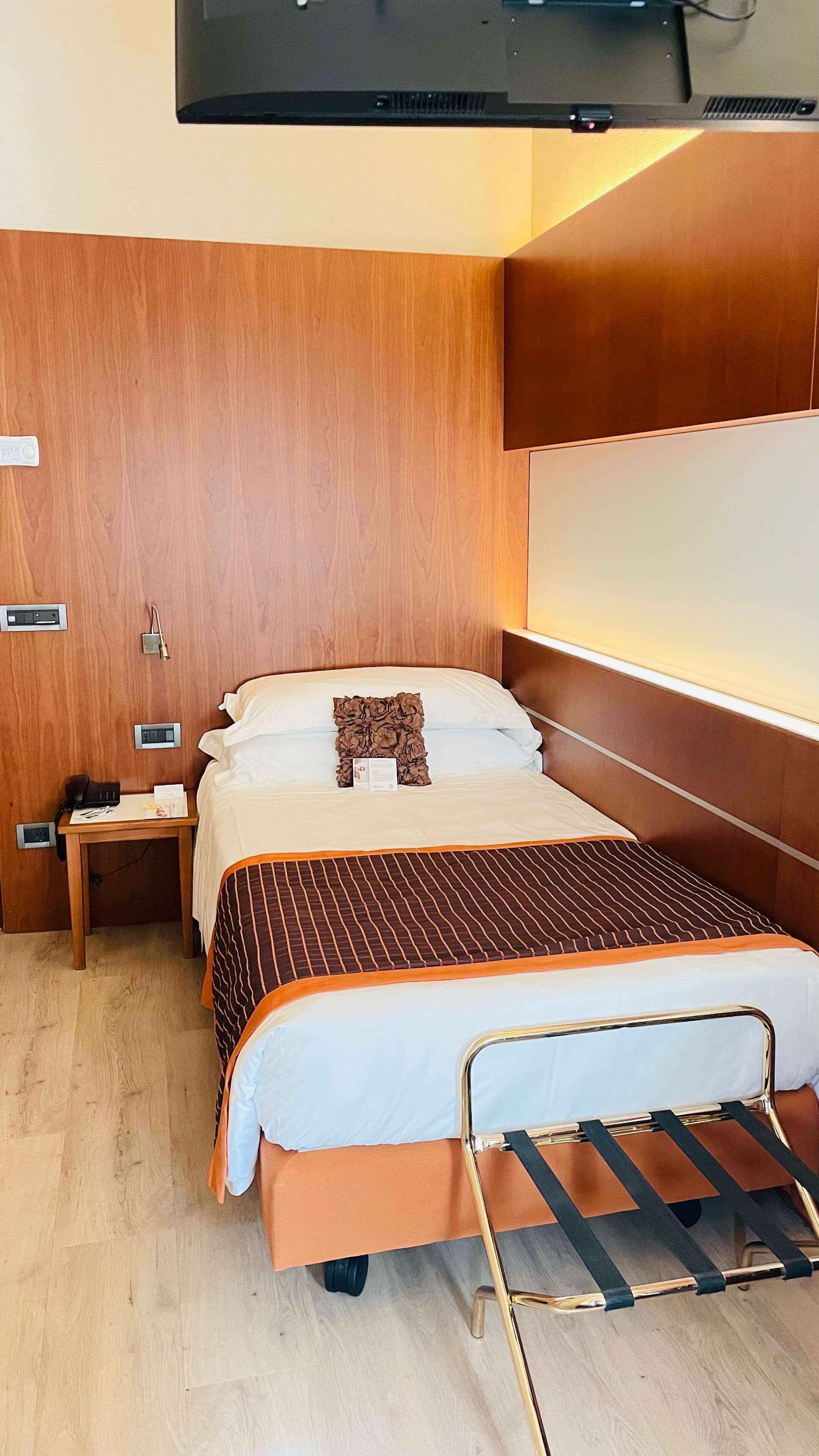 A modern hotel room with a bed, bedside table, and a TV mounted on the wall.
