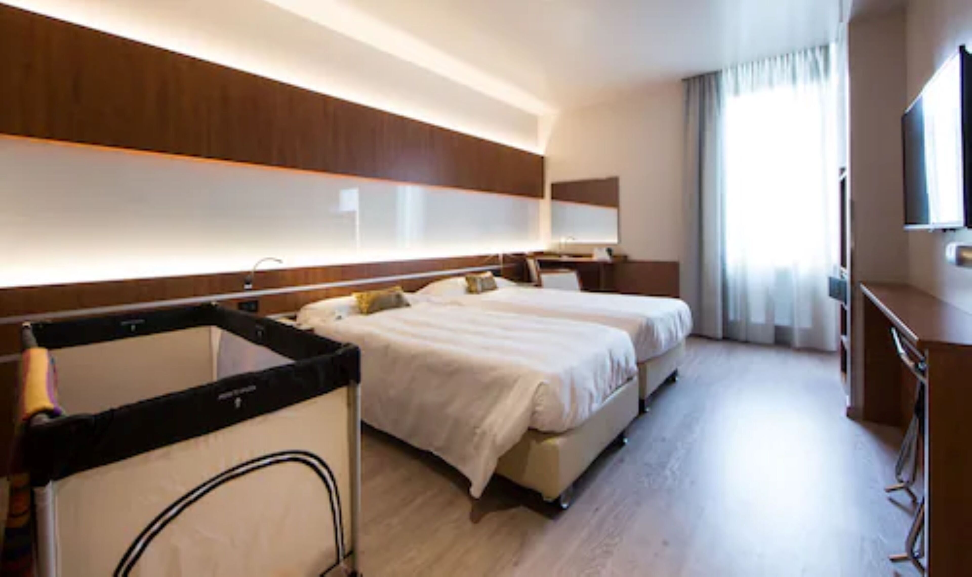 A hotel room with two beds, a large mirror, a flat-screen TV, and a wooden floor.