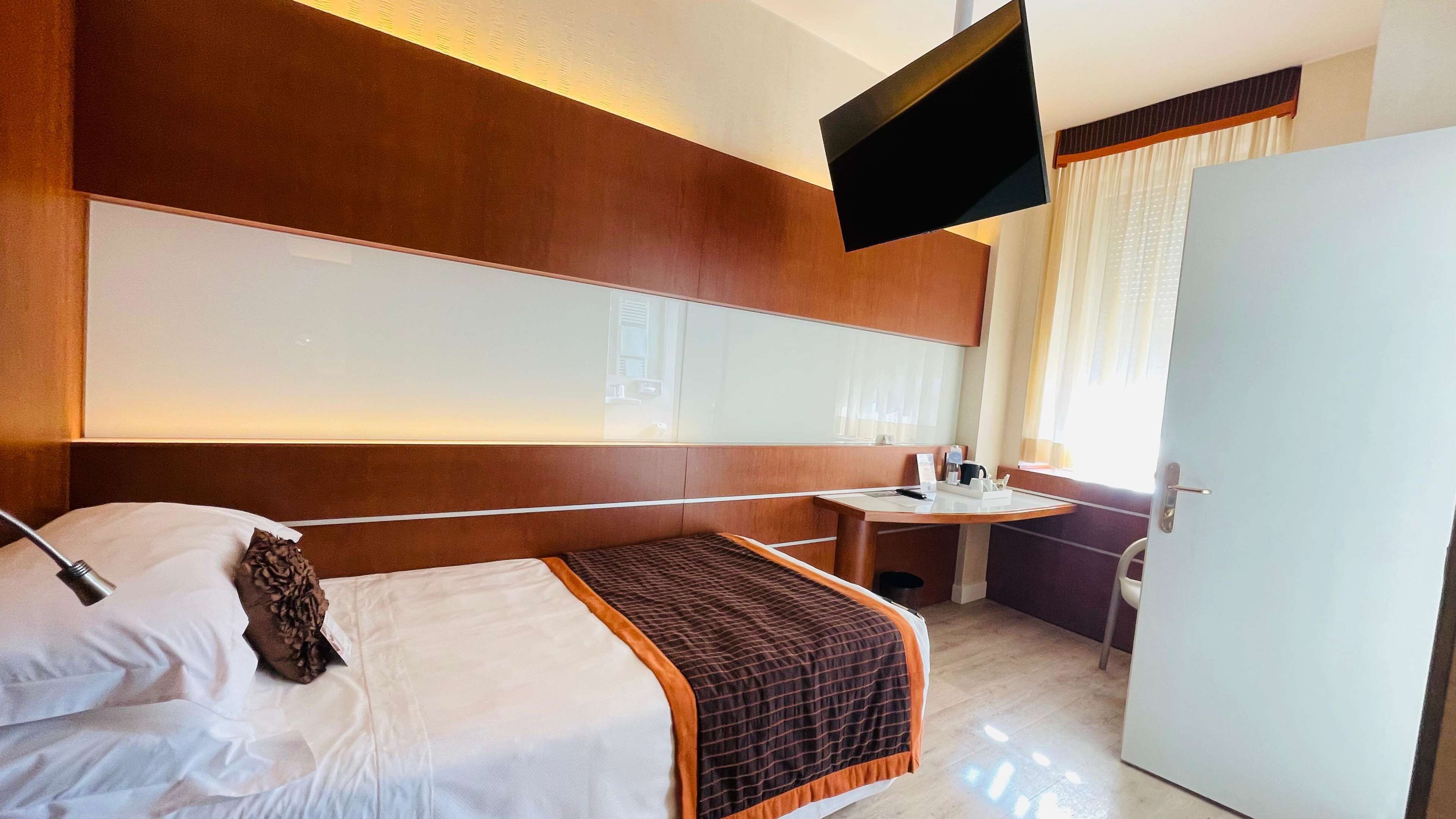 Una habitación de hotel con una cama, una mesita de noche y un televisor montado en la pared.