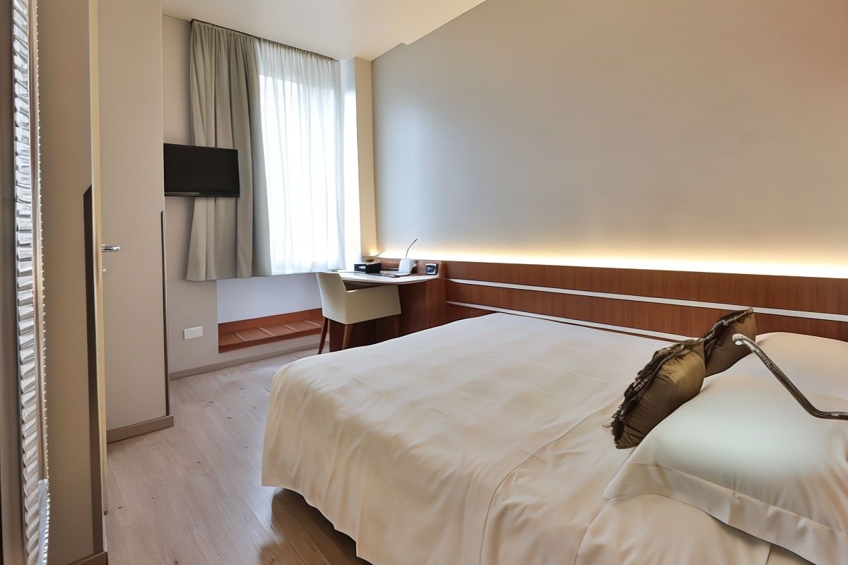 A hotel room with a bed, a desk, a chair, a television, and a bedside table.