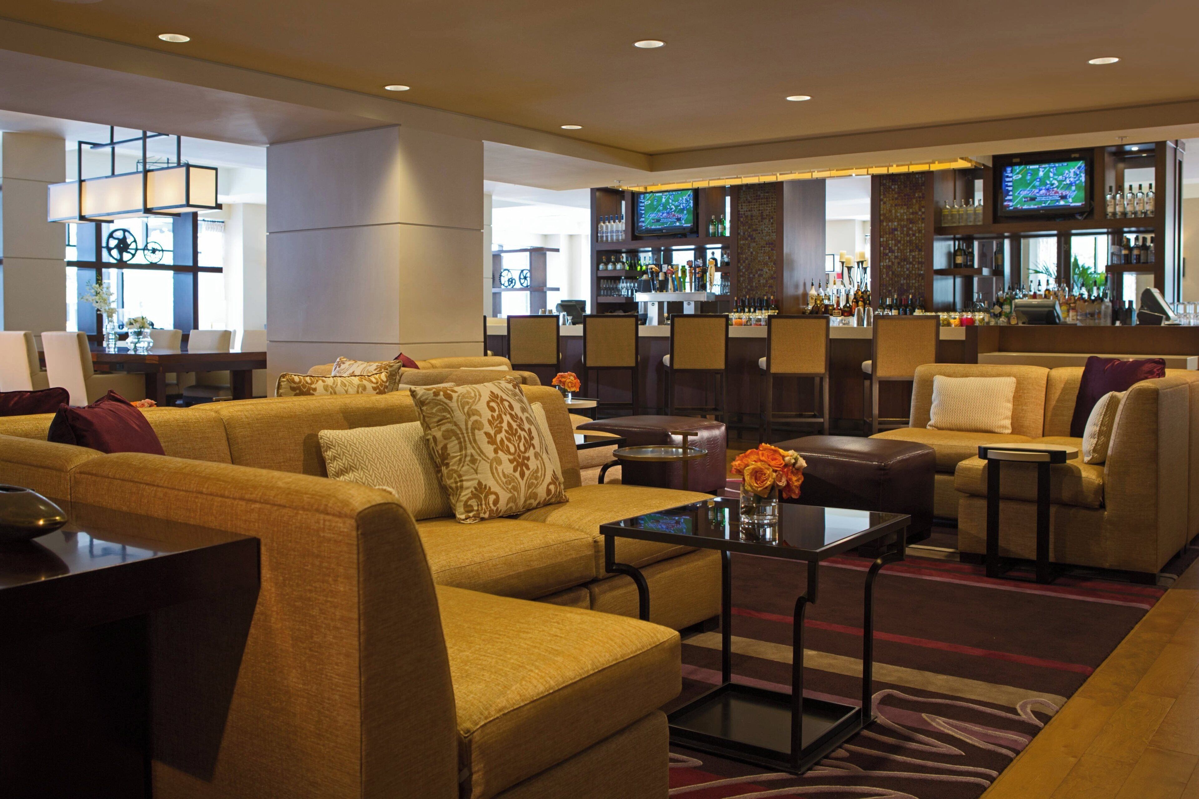 Eine Hotelhalle mit mehreren Sofas, einer Bar und einem Fernsehbildschirm.