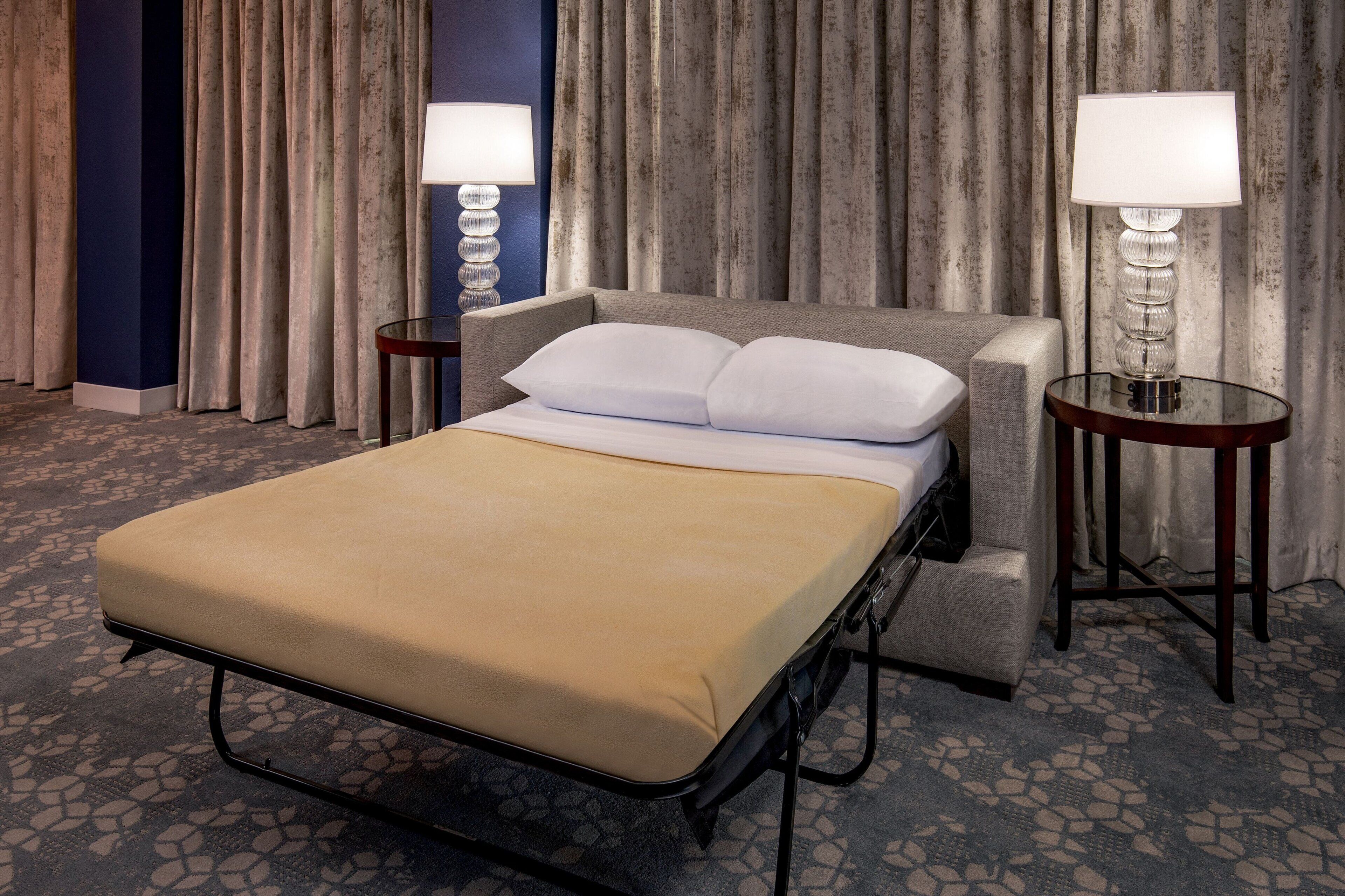 A hotel room with a bed, two bedside tables, a lamp, and a curtain backdrop.