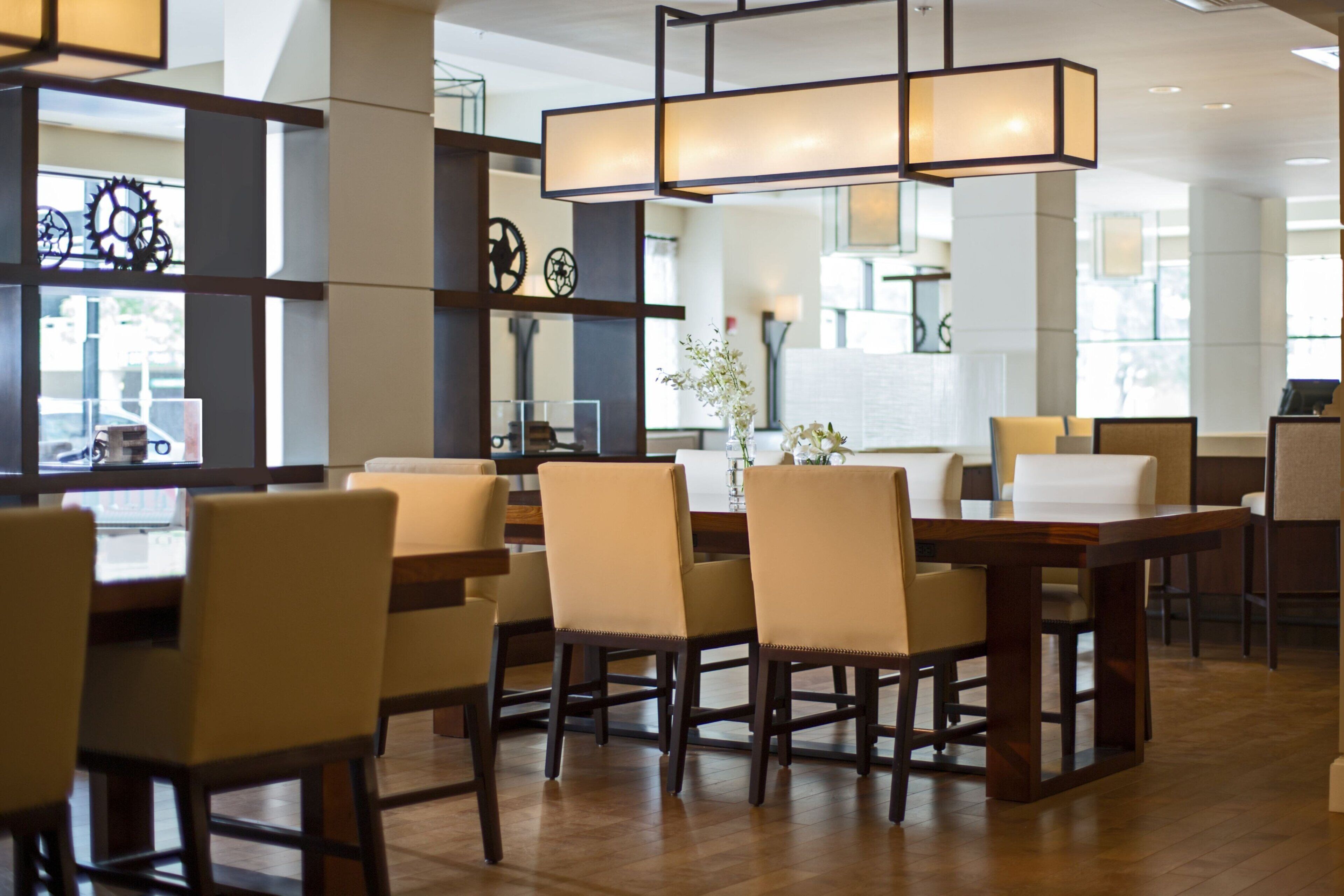 A modern dining area with wooden tables and chairs, a central light fixture, and decorative wall elements.