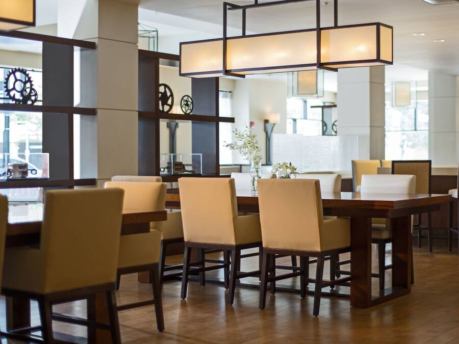 A modern dining area with wooden tables and chairs, a central light fixture, and decorative wall elements.