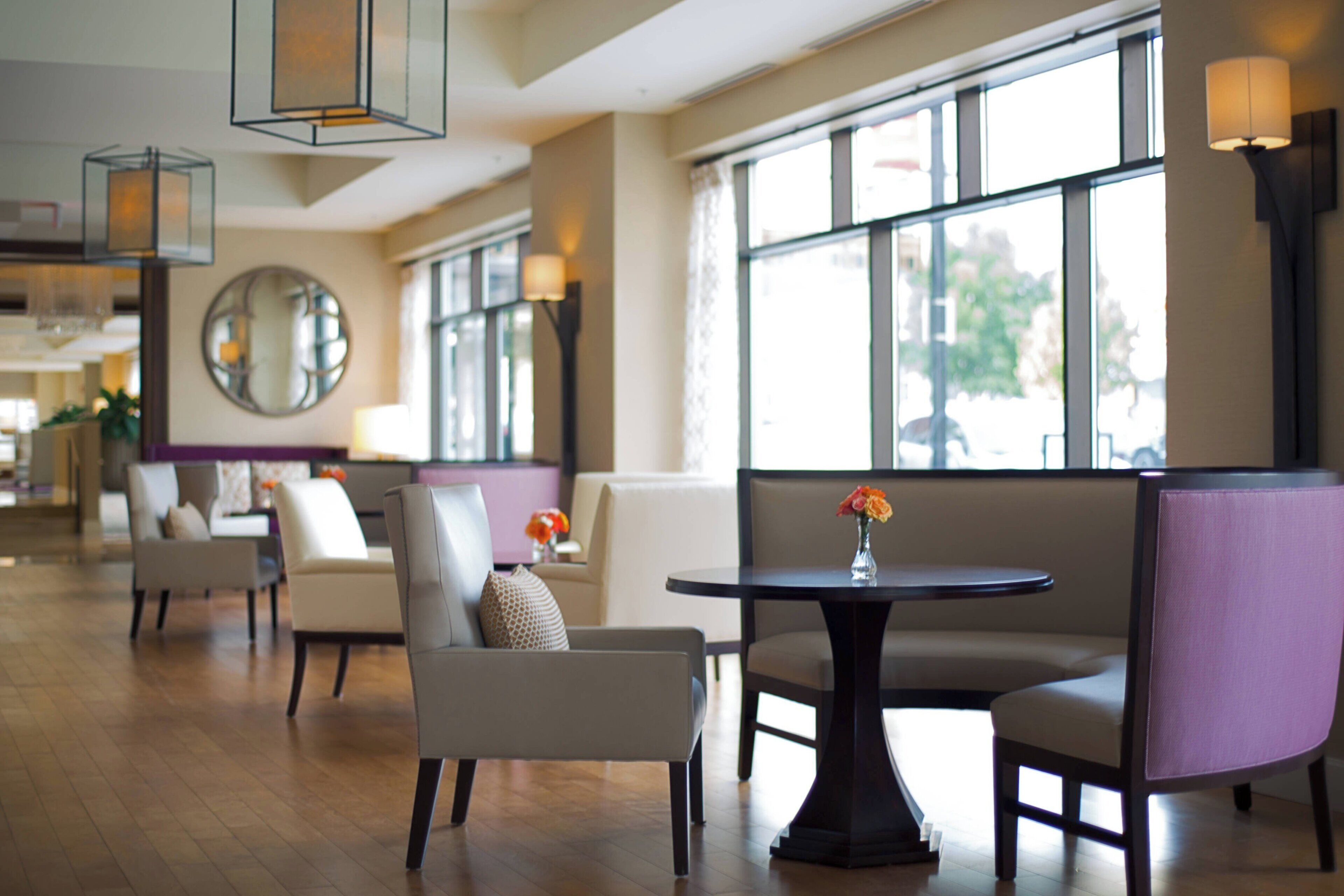 A modern hotel lobby with a round table, seating area, and large windows.
