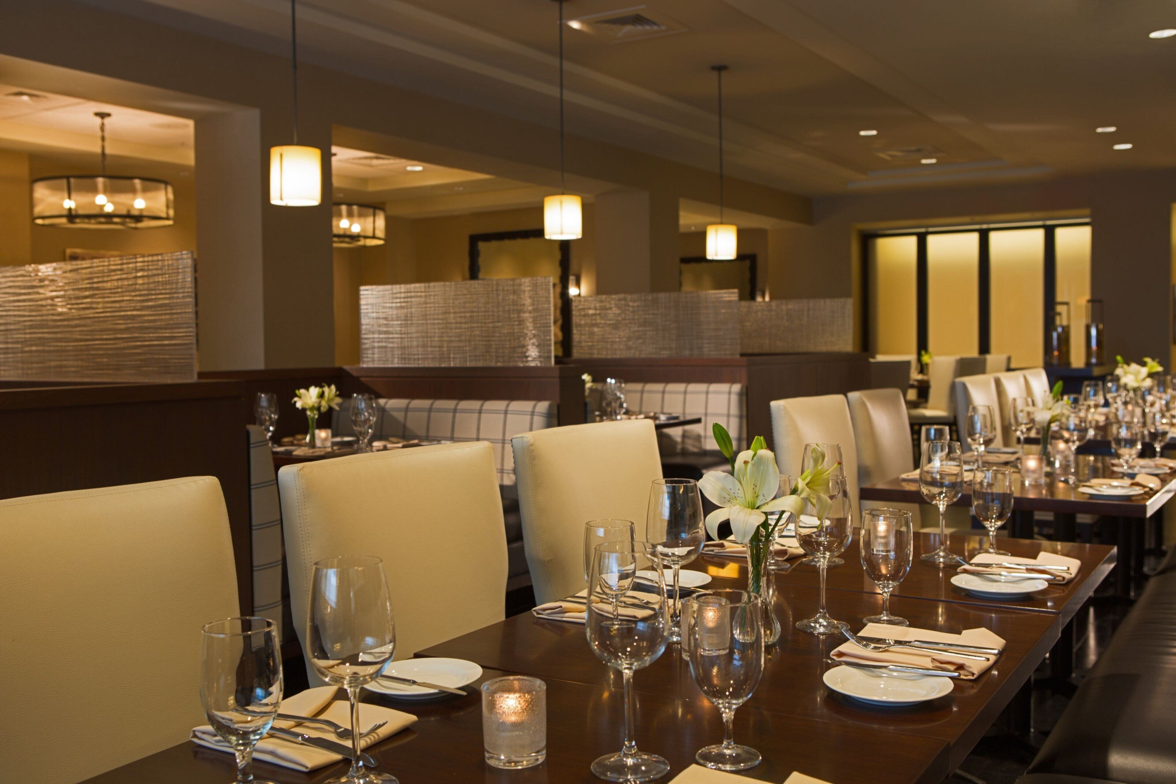 A restaurant with long tables set for dining, featuring candles, wine glasses, and white flowers.