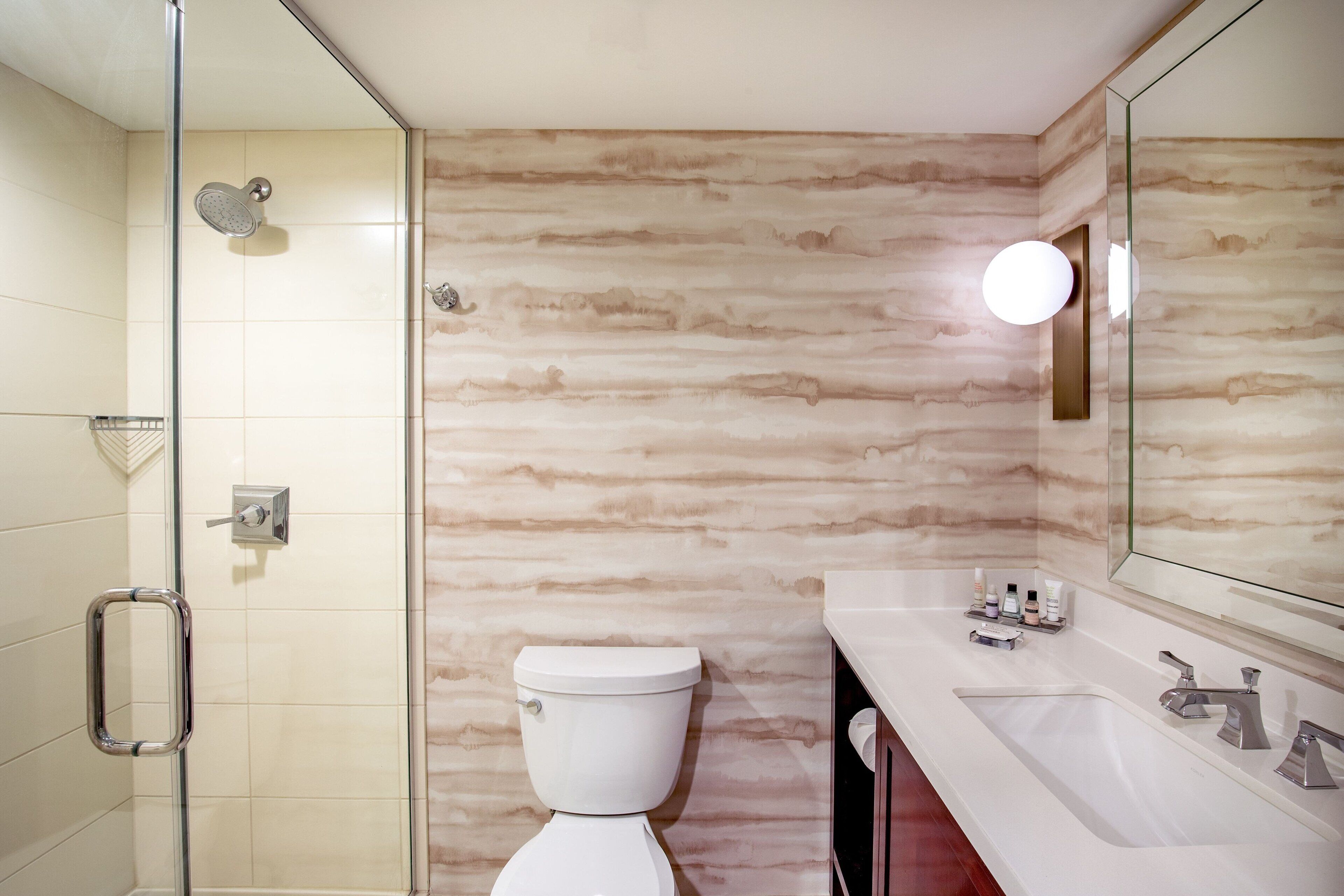 Een moderne badkamer met een douchecabine van glas, een wit toilet en een grote spiegel boven de wastafel.