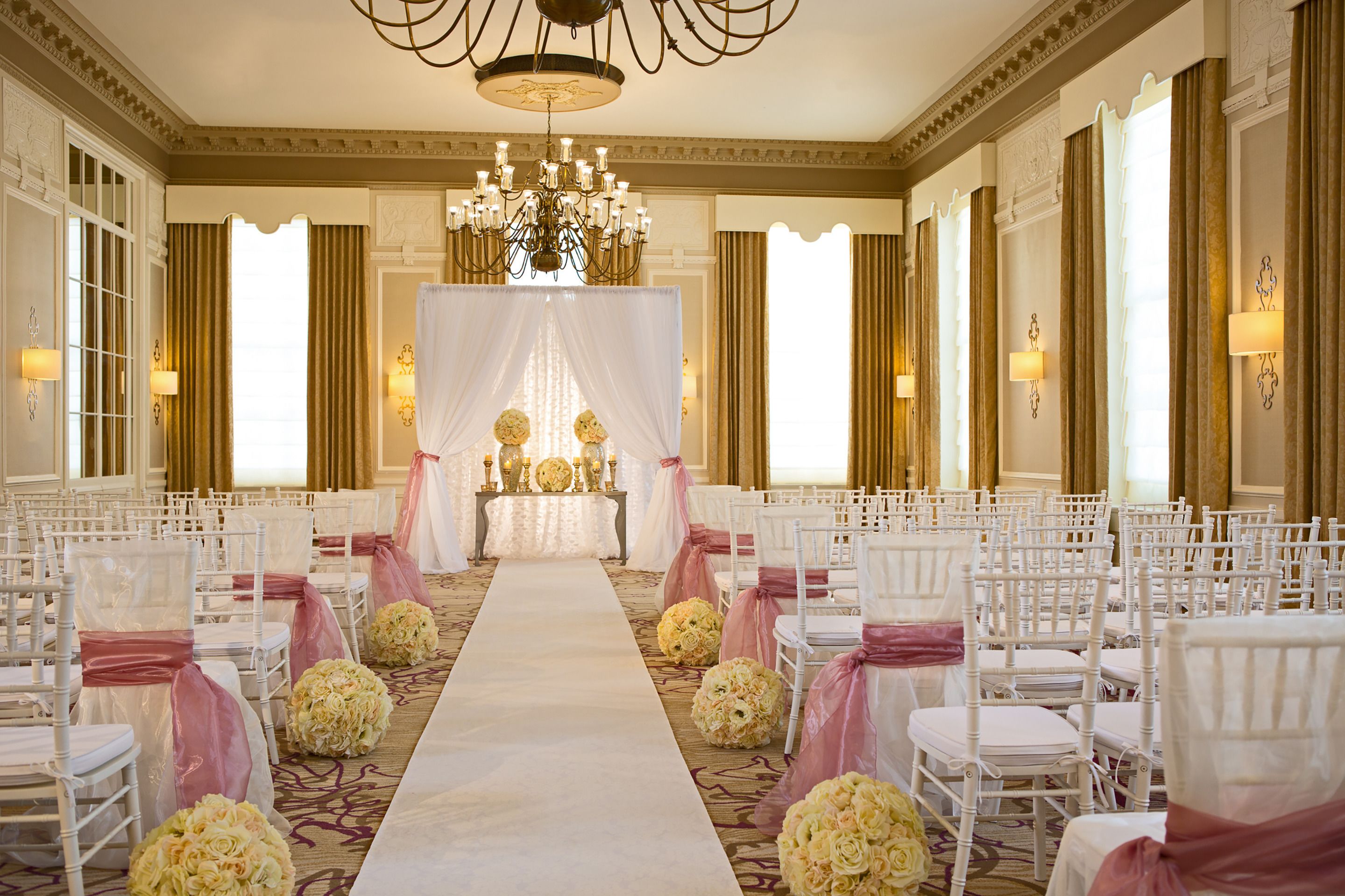 Un espace événementiel élégant, avec des rangées de chaises blanches, une allée centrale et des compositions florales.