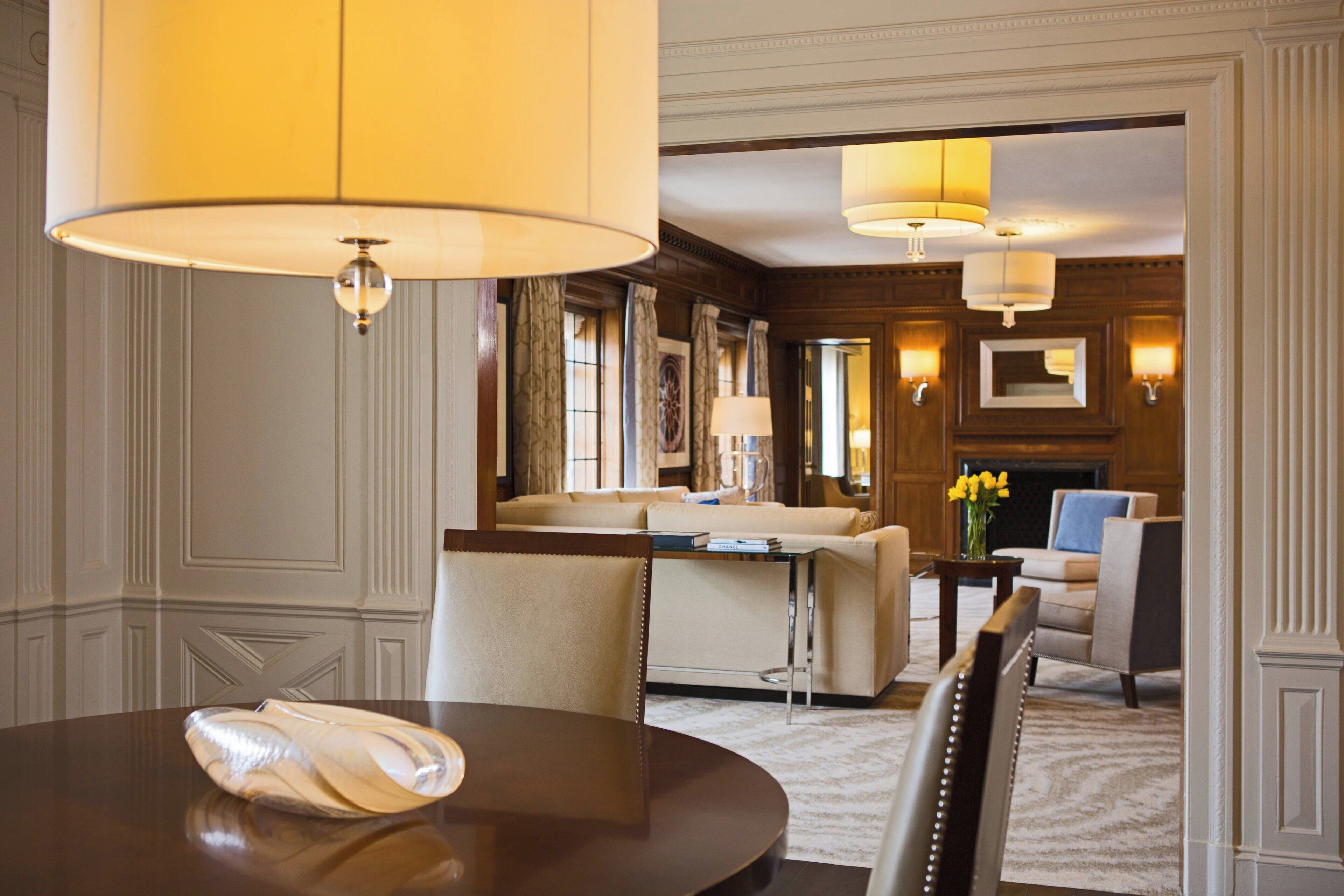 A hotel room with a round dining table, a sofa, a chair, and a fireplace.