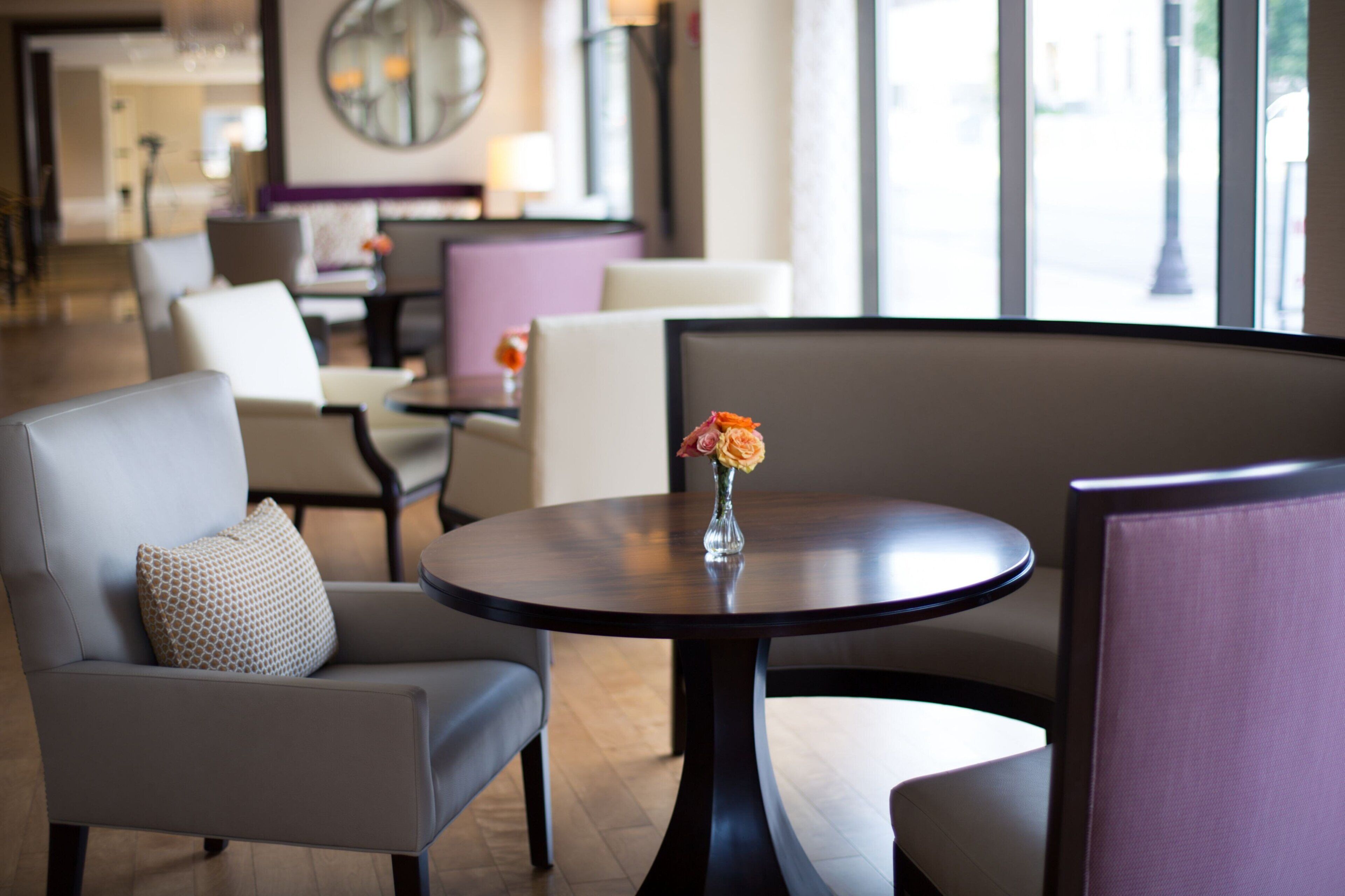 A modern hotel lobby with a round table, comfortable seating, and a vase with flowers.