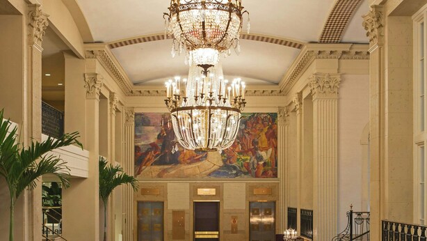 Un vaste hall d’entrée agrémenté d’un grand lustre, d’une fresque murale et d’un tapis à motifs.