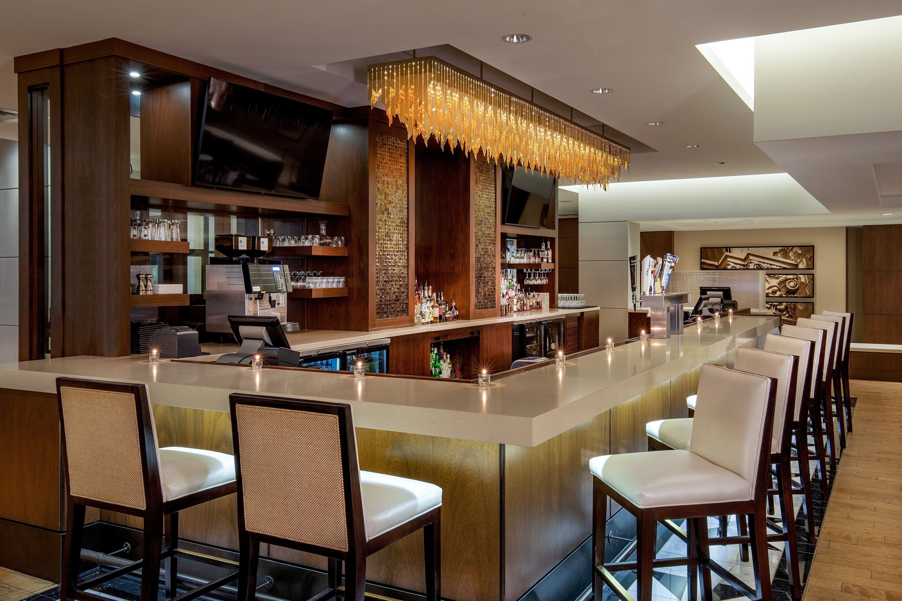A modern bar area with a long counter, bar stools, and a television mounted on the wall.