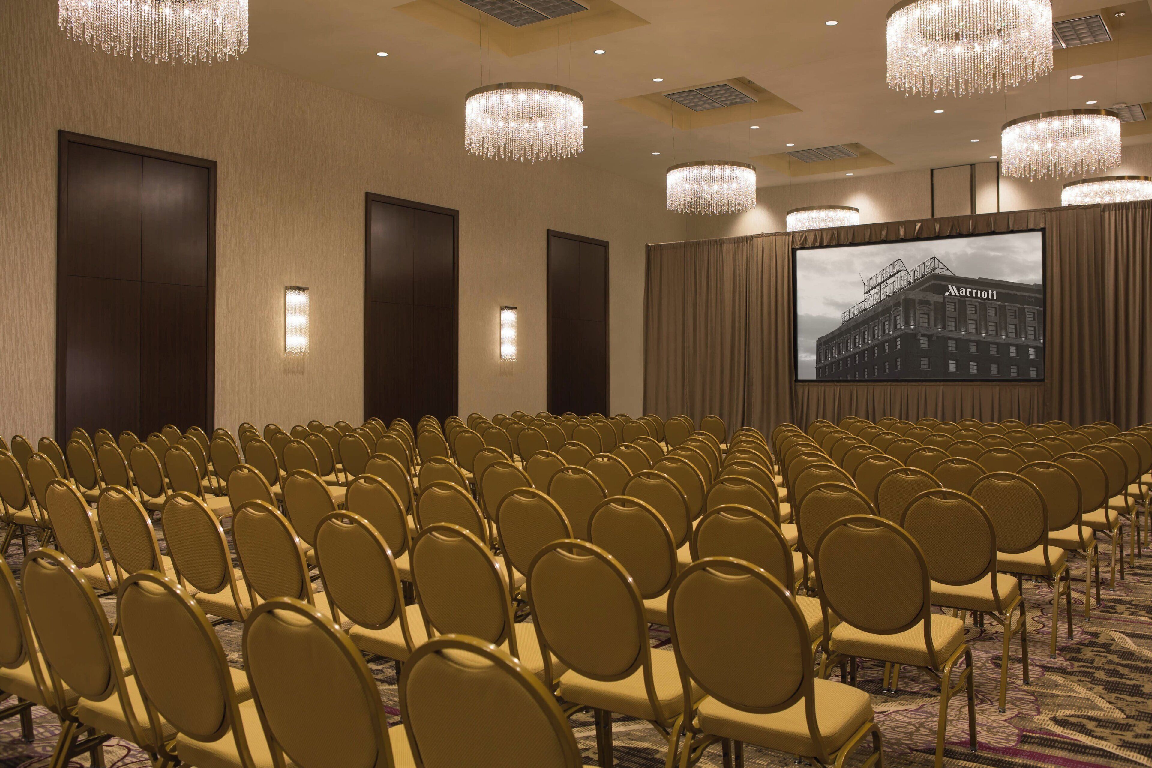 A conference room with rows of chairs, a large screen, and chandeliers.