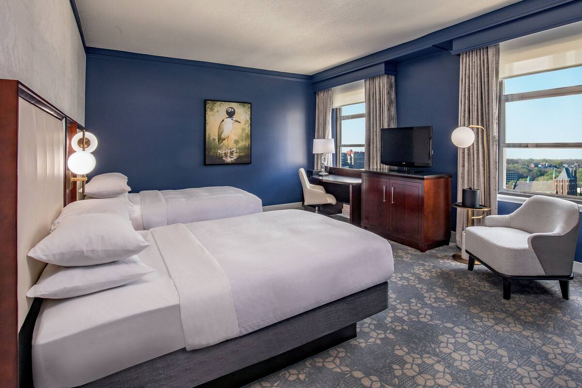 Habitación de hotel con una cama grande, un escritorio, una silla, un televisor y vistas a la ciudad.