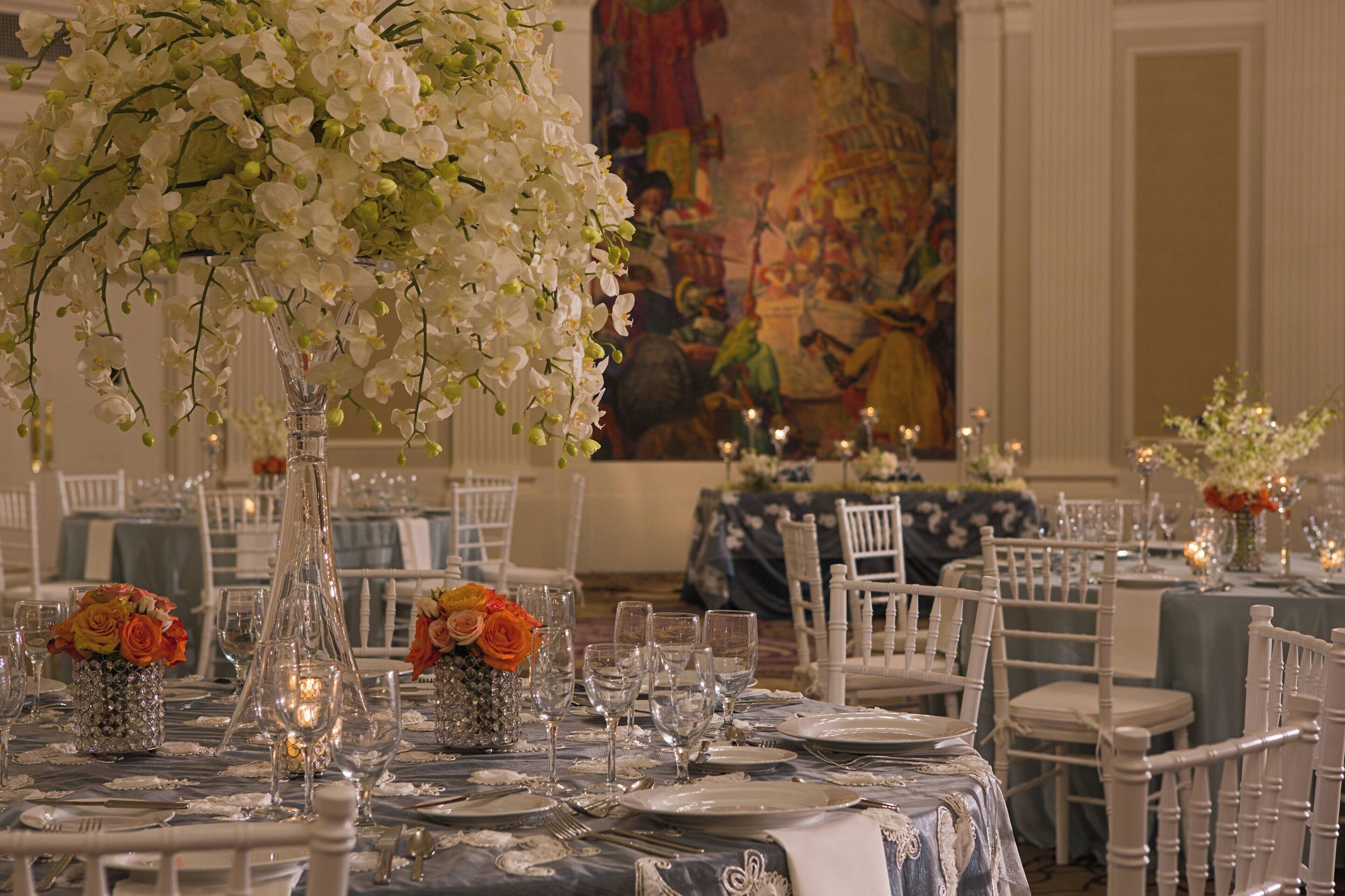 A banquet hall with tables set for a formal event, featuring floral centerpieces and candle lighting.