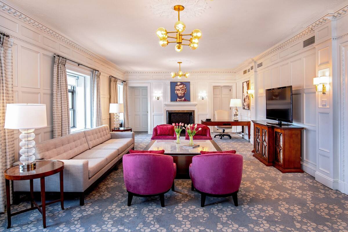 Een ruime woonkamer met een bank, twee fauteuils, een salontafel en een open haard.