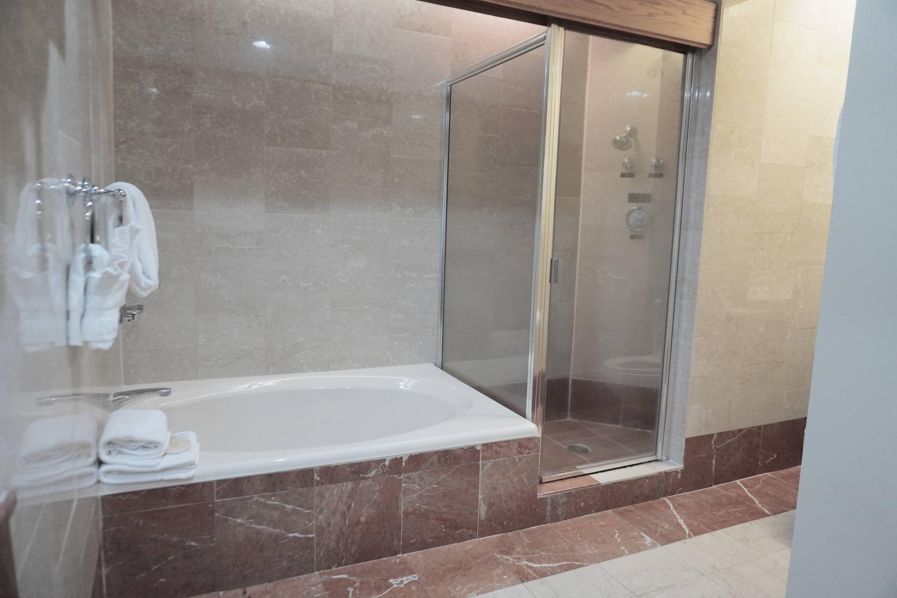 A modern bathroom with a glass-enclosed shower, a white bathtub, and marble flooring.