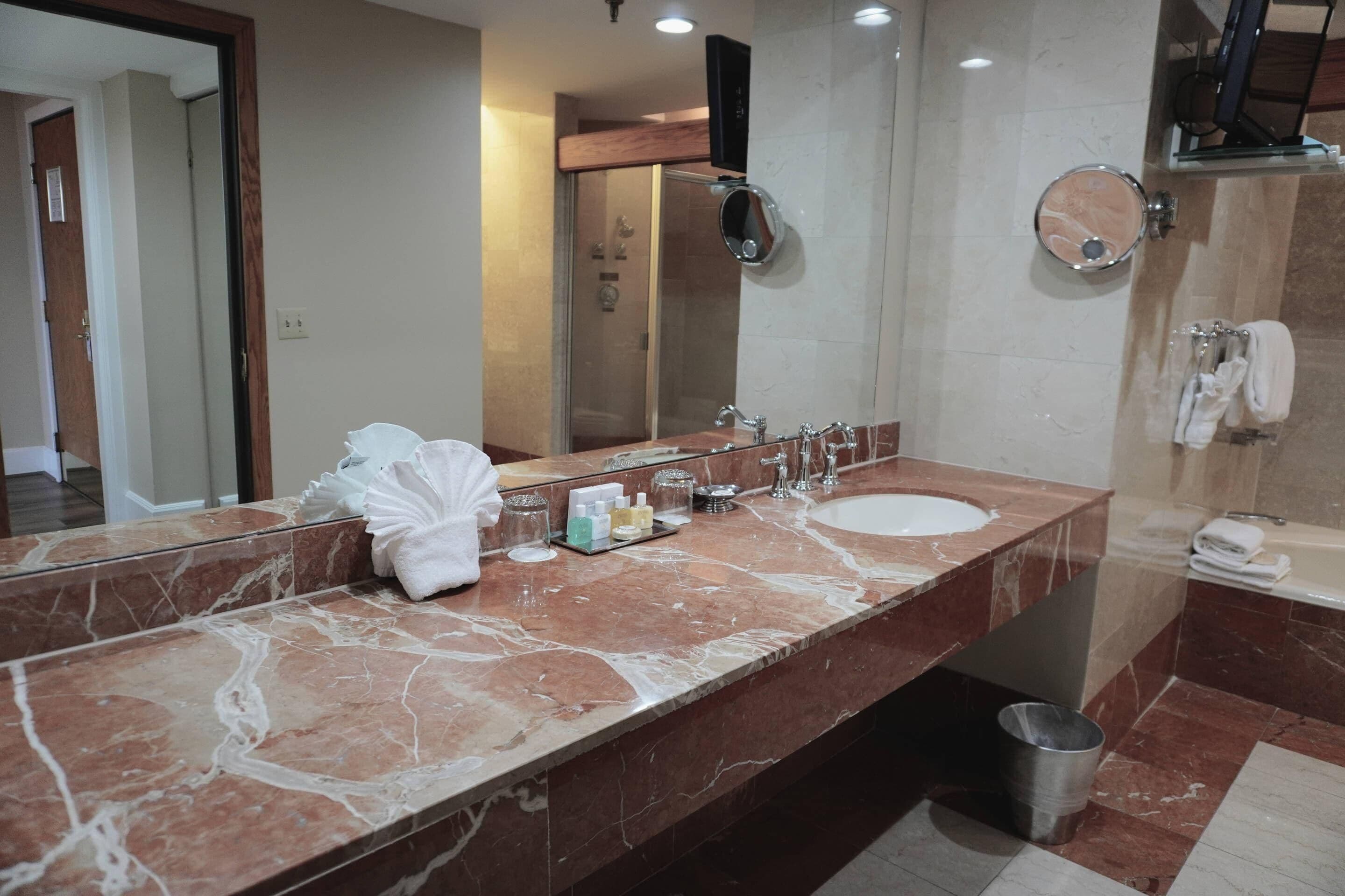 A bathroom with a marble vanity, a large mirror, a sink, a shower, and a toilet.
